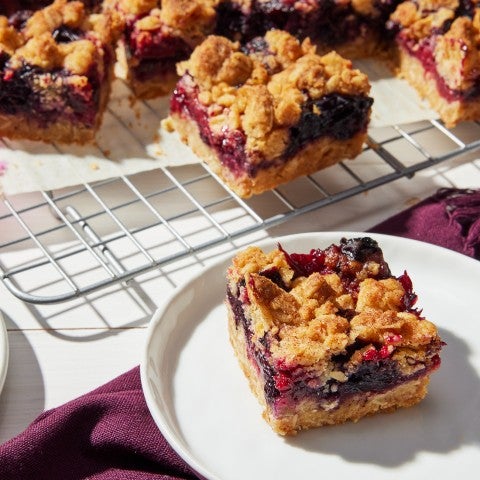 Photograph of a berry bar on a plate sliced into a square with layers of crumb, berries, and crust. - select to zoom