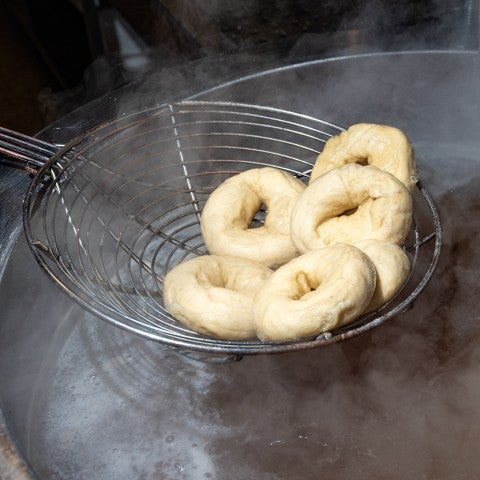 A wire ladle pulling bagels from a pot of boiling water. - select to zoom