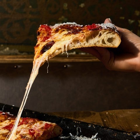Photograph of a handing raising a slice of pizza with cheese stretching down to the rest of the pie. - select to zoom