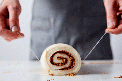 A baker using a piece of dental floss to cut the log of cinnamon roll dough into 8 sections.