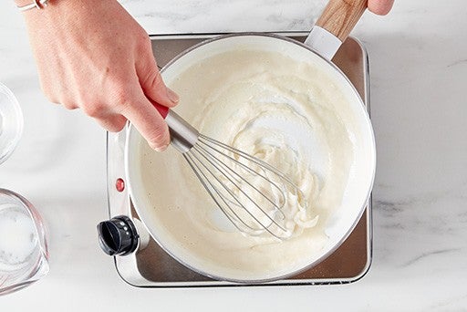 Baker whisking a mixture of flour and milk together over a burner to make a roux.