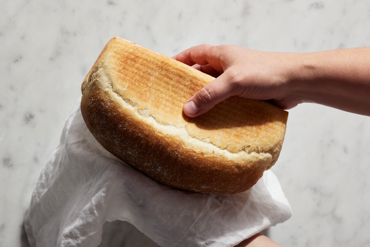 Baker squeezing a loaf of baked sandwich bread