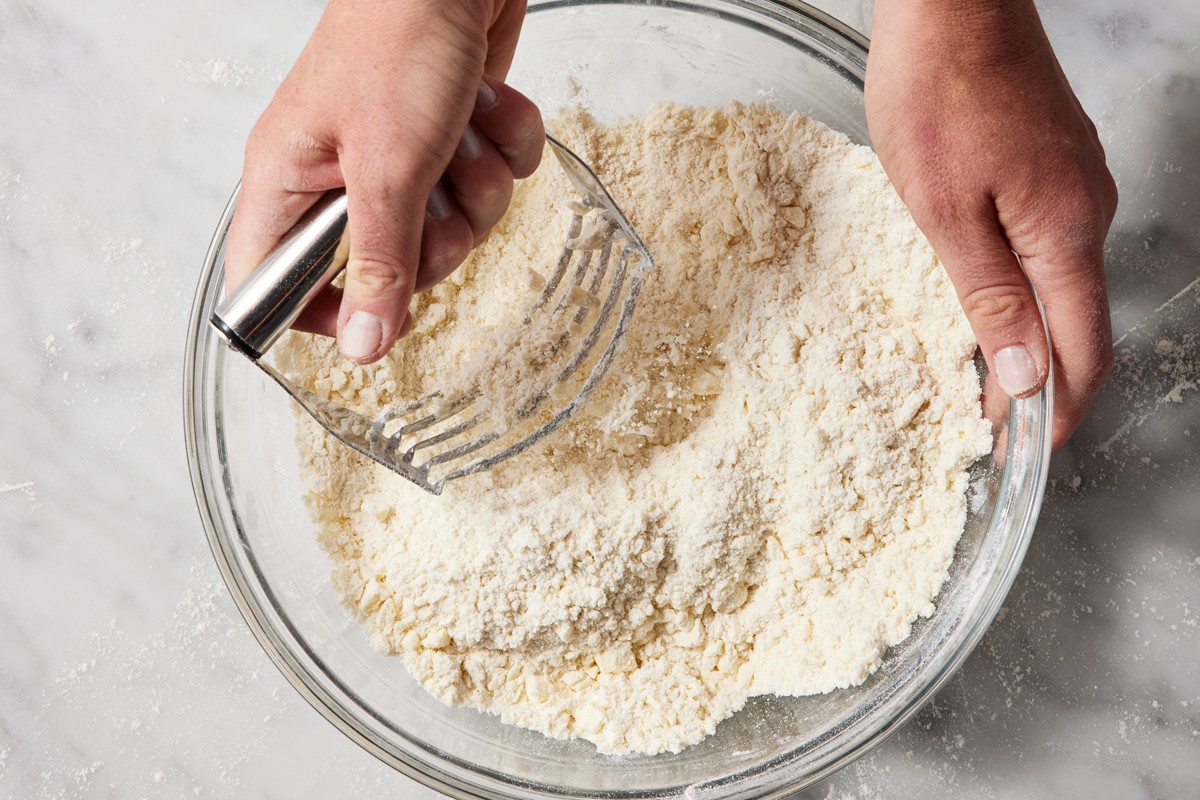 Hands using pastry cutter to cut butter into flour