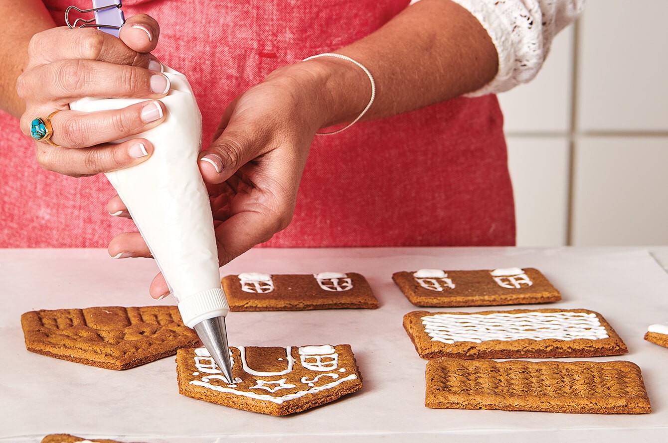A baker ices details onto a piece of a gingerbread house