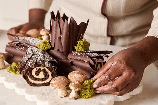 Gently placing macha "moss" onto a white platter holding a sculptural Chocolate Buche de Noel with Cookie Butter Whipped Ganache.
