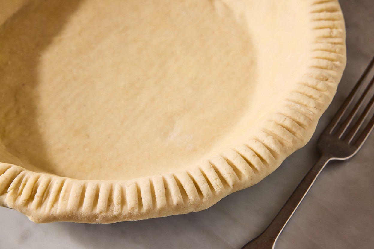 A gluten-free pie crust in a pie pan showing a smooth dough and a beautifully fork-crimped crust.
