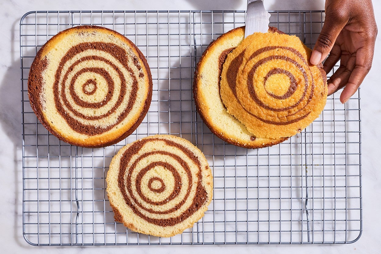 Souche de Noël fresh out of the oven on a baking rack with the slices cut off the top showing rings of vanilla and chocolate swirls.