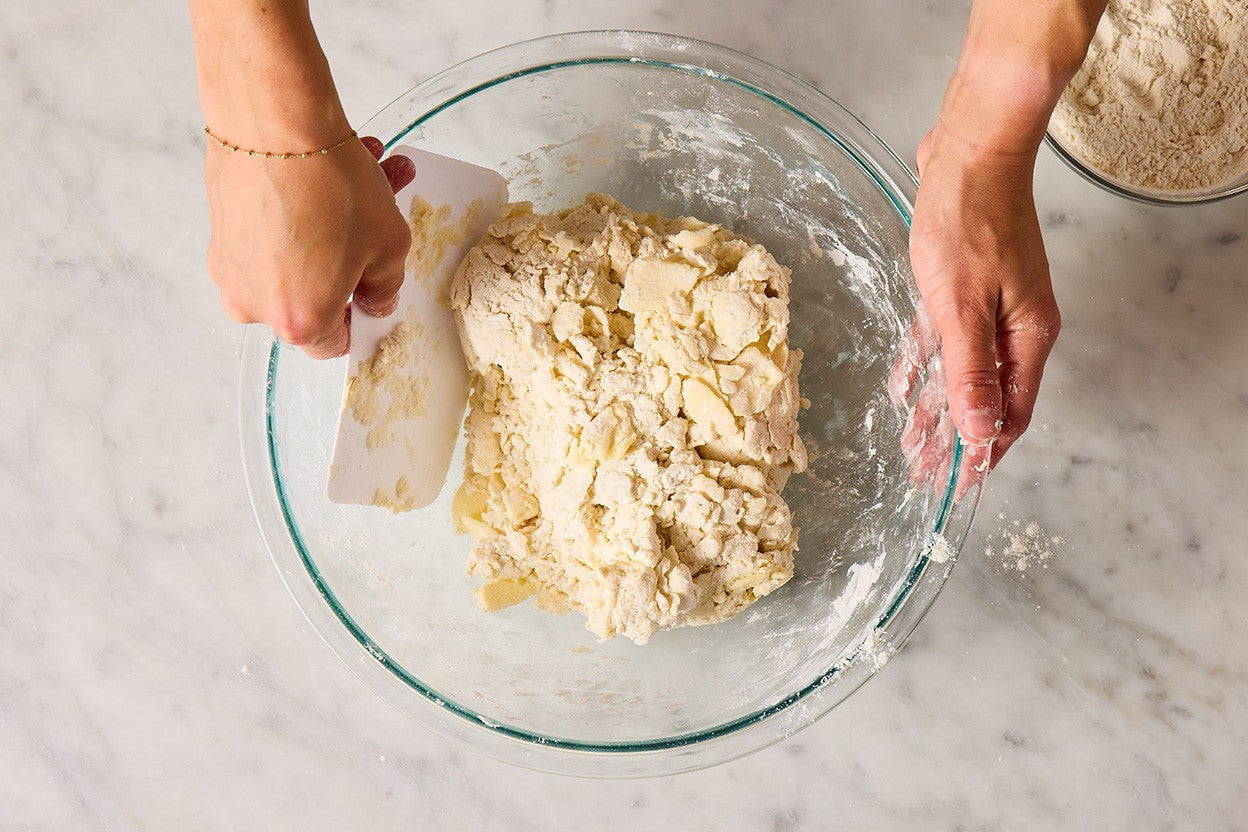 Using a bowl scraper to pull bits of dough mix from the insides of a bowl.
