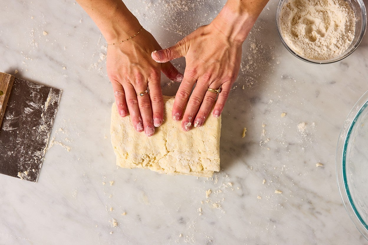 Hands pressing layers of biscuit dough together, seen from above.