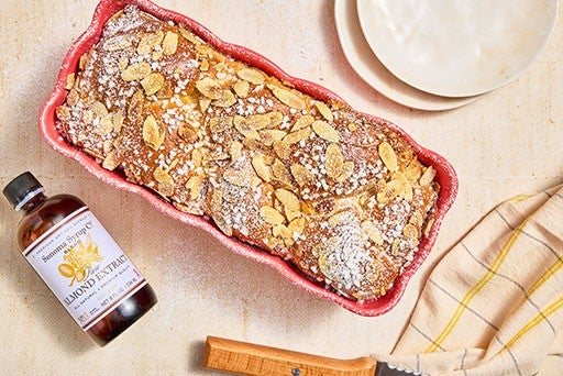 Almond Croissant Milk Bread shown in a Madeleine Loaf Pan on a counter with Sonoma Syrup Co. Almond Extract next to it.