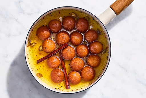 Gulab Jamun in a pot of syrup with fragrant spices.