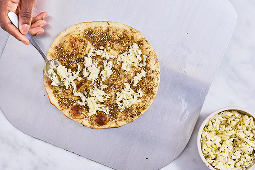 Adding toppings to Zaatar Manakeesh before baking.
