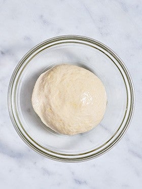 Flatbread dough in a clear bowl before rising.