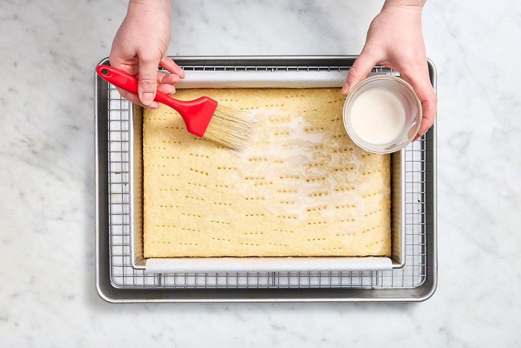 Brushing coconut cream onto a docked coconut sheet cake.