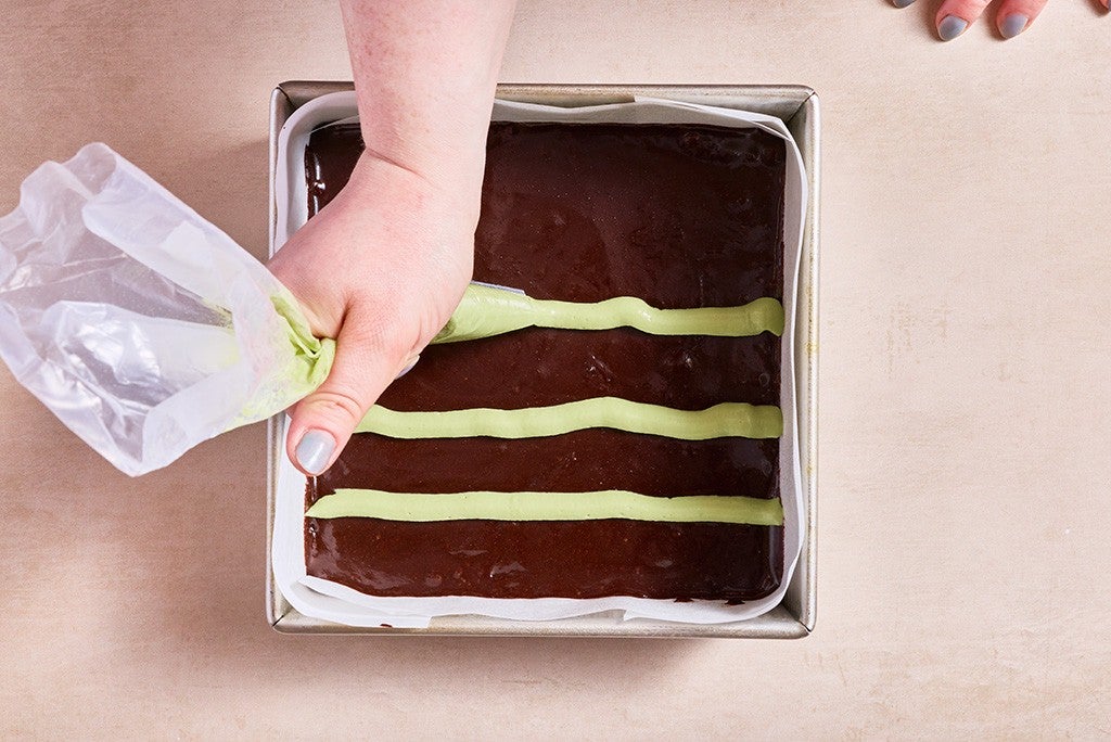 Piping mint topping onto a pan of brownies.