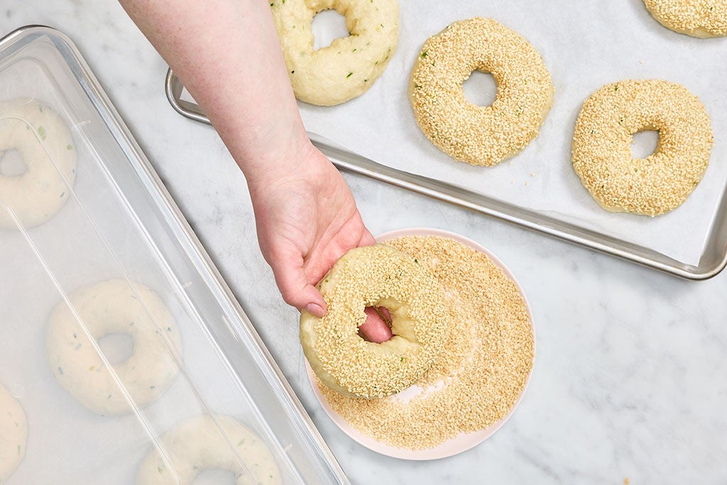 Dipping freshly boiled Sesame Sourdough Discard Bagels into sesame seeds prior to baking.