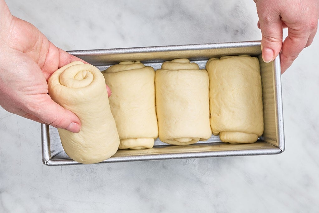 Placing rolled up Sourdough Milk Bread dough into a pullman pan