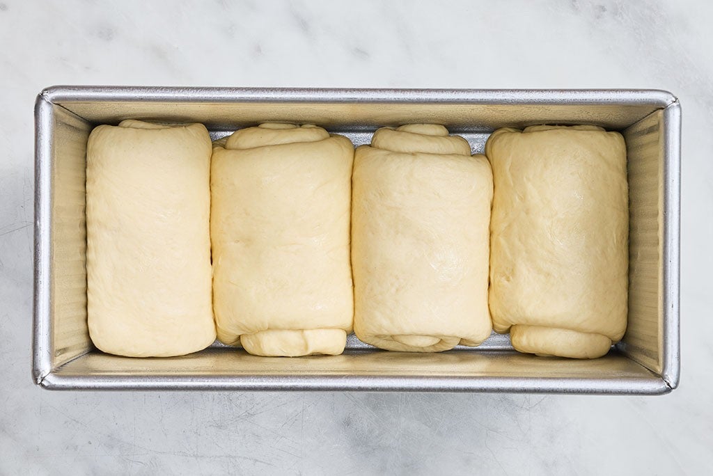 A pullman pan filled with rolled up Sourdough Milk Bread dough