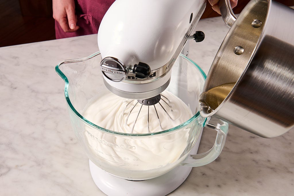 Mixing Italian Buttercream with a whisk attachment on a stand mixer while adding liquid