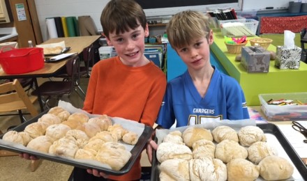 Two children, each holding a baking sheet of rolls