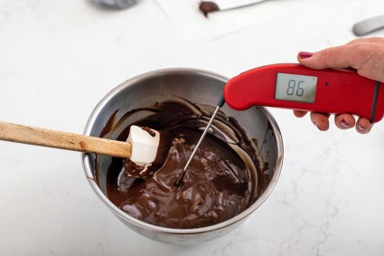 A baker testing the temperature of a bowl of melted chocolate; it reads 86 degrees.