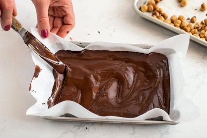 A baker using an offset spatula to spread tempered chocolate on a small baking sheet