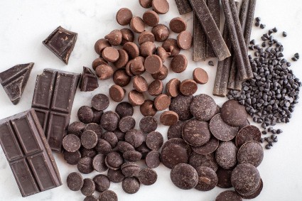 A mix of different kinds of chocolate on a table including chocolate chips, chopped chocolate, and chocolate bars