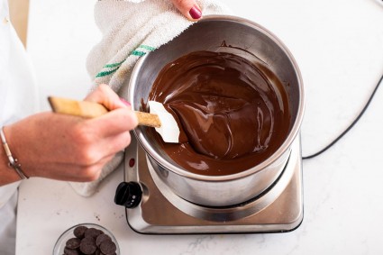 A baker stirring a bowl of melted chocolate over a double boiler