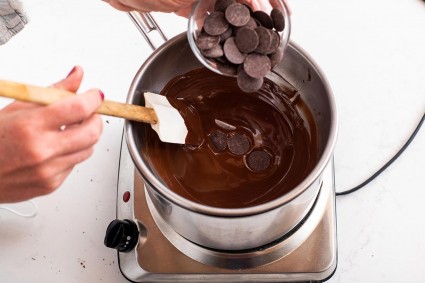 A baker adding seed chocolate to melted chocolate over a double boiler