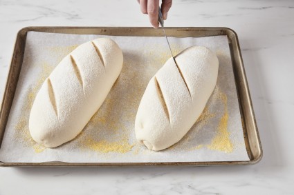 Baker scores two loaves of shaped bread dough
