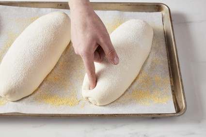 Baker using one finger to press risen bread dough loaf