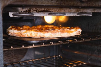 Pizza baking in an oven on the top rack close to the broiler