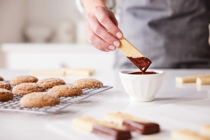 A baker dipping a stick of shortbread into tempered chocolate