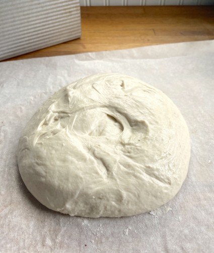 Mound of yeast dough on a piece of parchment, pre-shaped into a rough round.