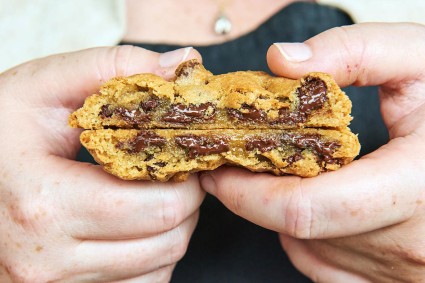 Hands holding chocolate chip cookie cut in half to show interior