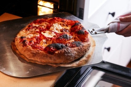 Baked pizza being removed from oven with baking peel