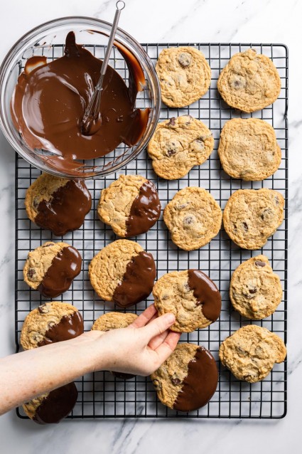 Peanut butter chocolate chip cookies that have been dipped into tempering chocolate, resting on a cooling rack