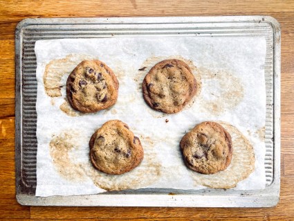 Four baked chocolate chip cookies on a parchment-lined baking sheet.