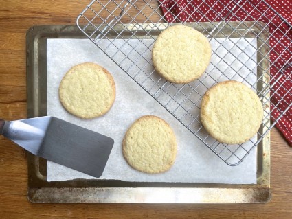 Four sweet Corn Cookies cooling, two on a cooling rack, two on a parchment-lined baking sheet.