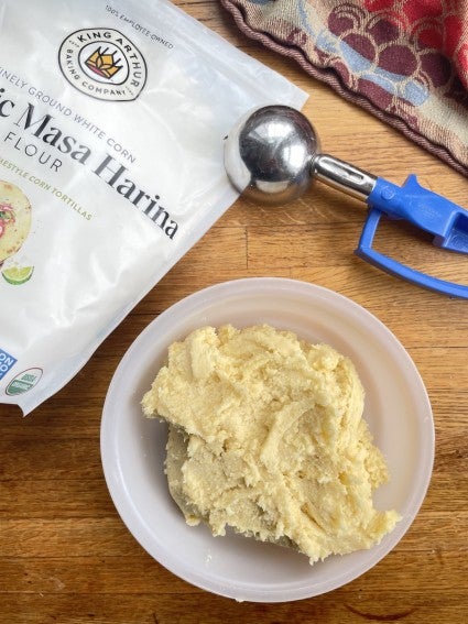 Batch of Sweet Corn Cookies dough in a plastic bowl with a cookie scoop and bag of masa harina flour.