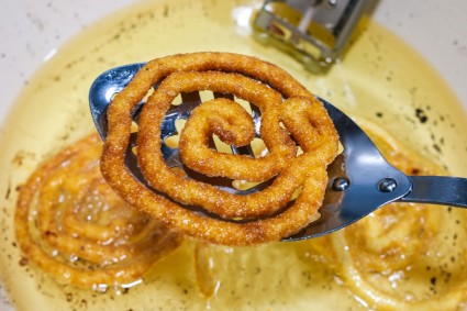 Jalebi being lifted out of hot oil with slotted spoon