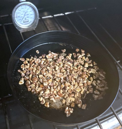 Toasted nuts in a blackened round cake pan on the shelf of an antique cast iron oven.