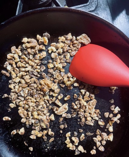 Nuts being stirred with a red silicone spatula in a blackened carbon steel pan.
