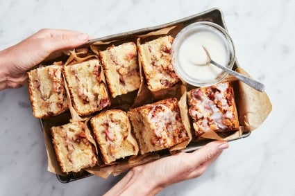 Slices of apple fritter cake in a serving box with bowl of glaze