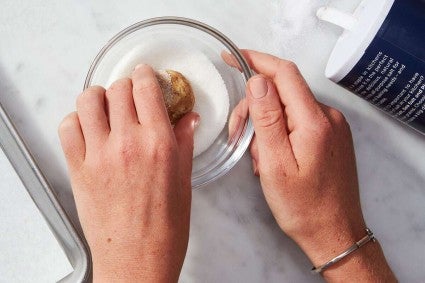 Cookie dough being rolled in bowl of sugar and salt mixture