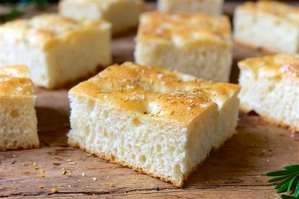 Fat focaccia cut in squares on a bread board.