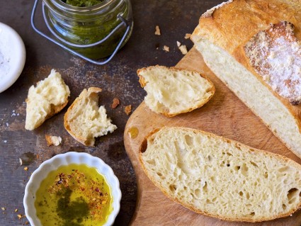 No-Knead Crusty White Bread sliced on a cutting board, with olive oil and herbs on the side.