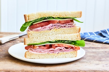 Cross section of stacked sandwich halves: cold cuts, tomato, cheese, and lettuce on white sandwich bread.