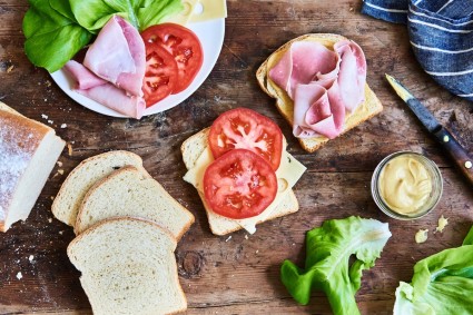 Classic Sandwich Bread being made into cold cut, lettuce, cheese, and tomato sandwiches on a wooden table top.