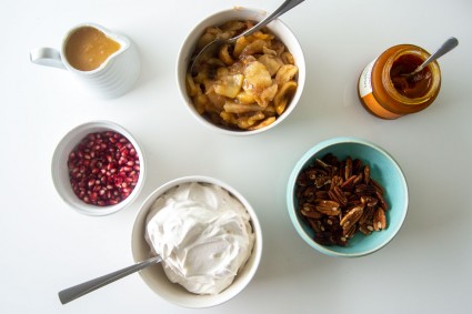 Bowls of pavlova toppings, including whipped cream, nuts, baked apples, and more
